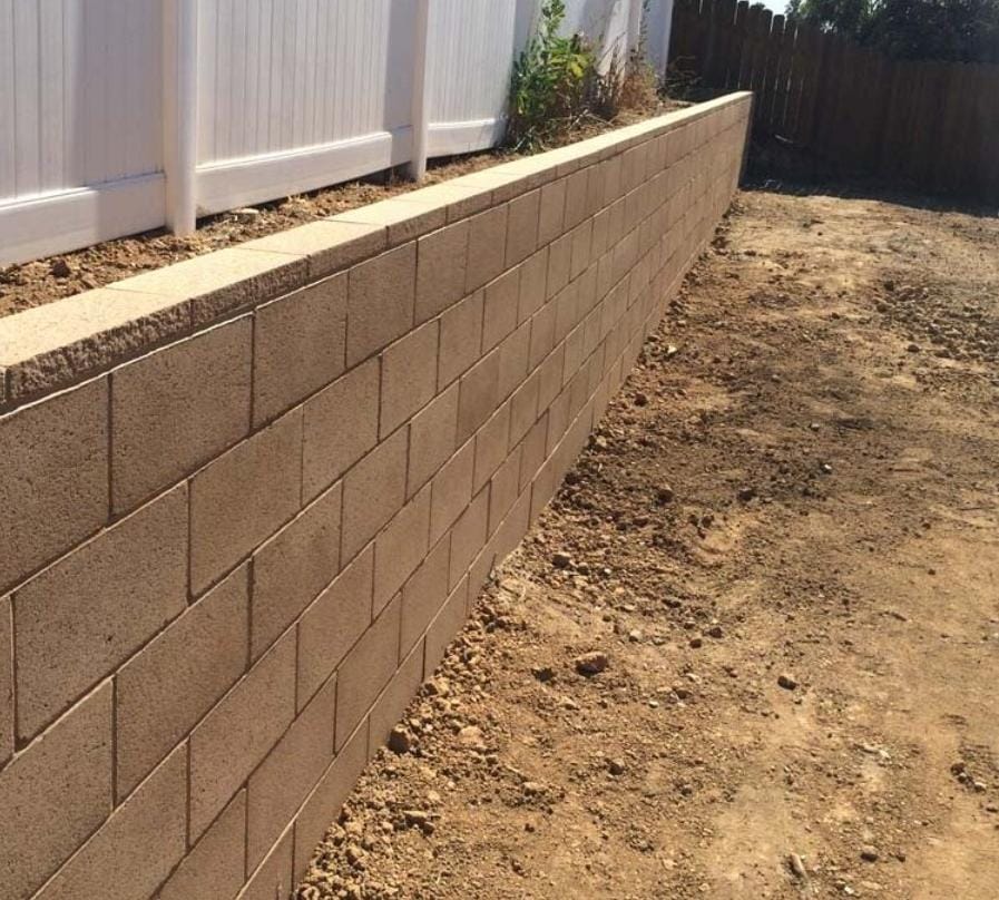 Straight tan retaining wall running along a backyard fence line