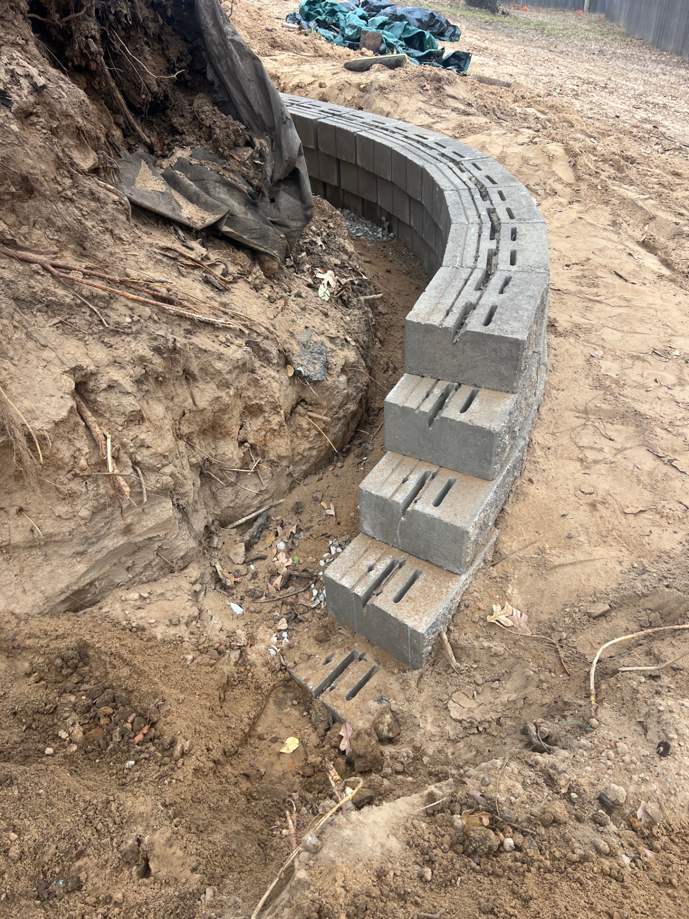 Curved gray concrete block retaining wall under construction on a slope